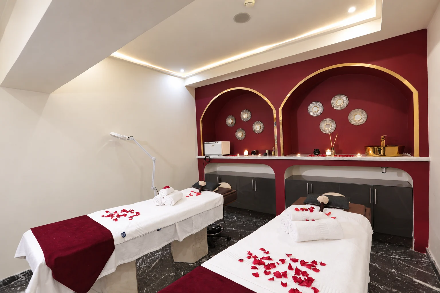 Cabine de massage à deux tables, alcôves bordeaux et touches dorées chez Orélia