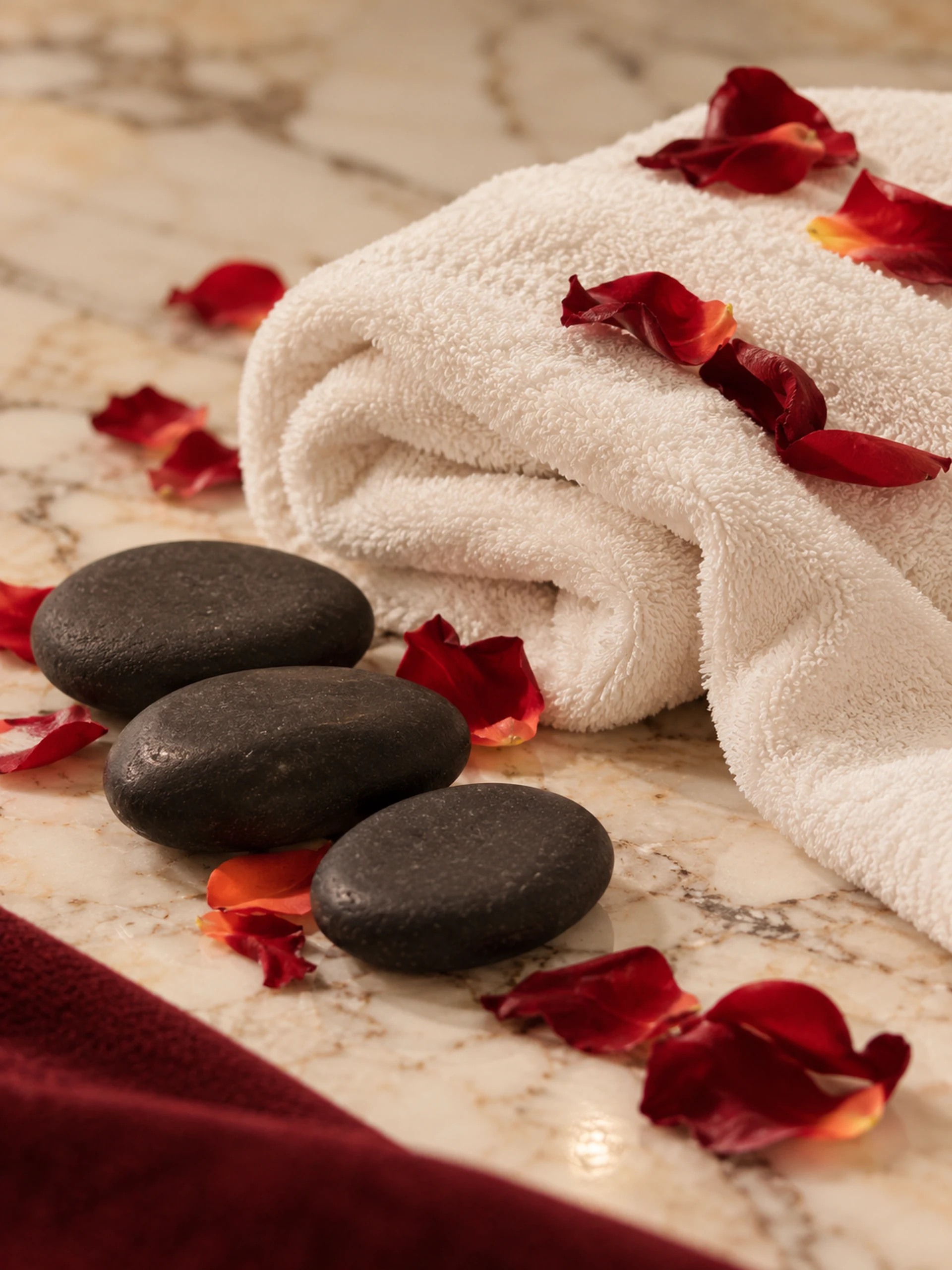 Ivory linen, massage stones and rose petals on pale marble