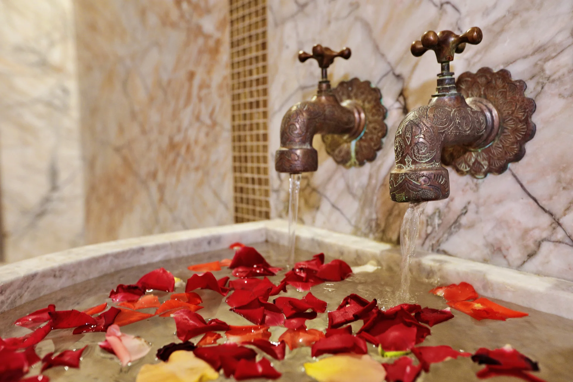 Robinetterie traditionnelle et pétales dans la vasque en marbre du hammam Orélia